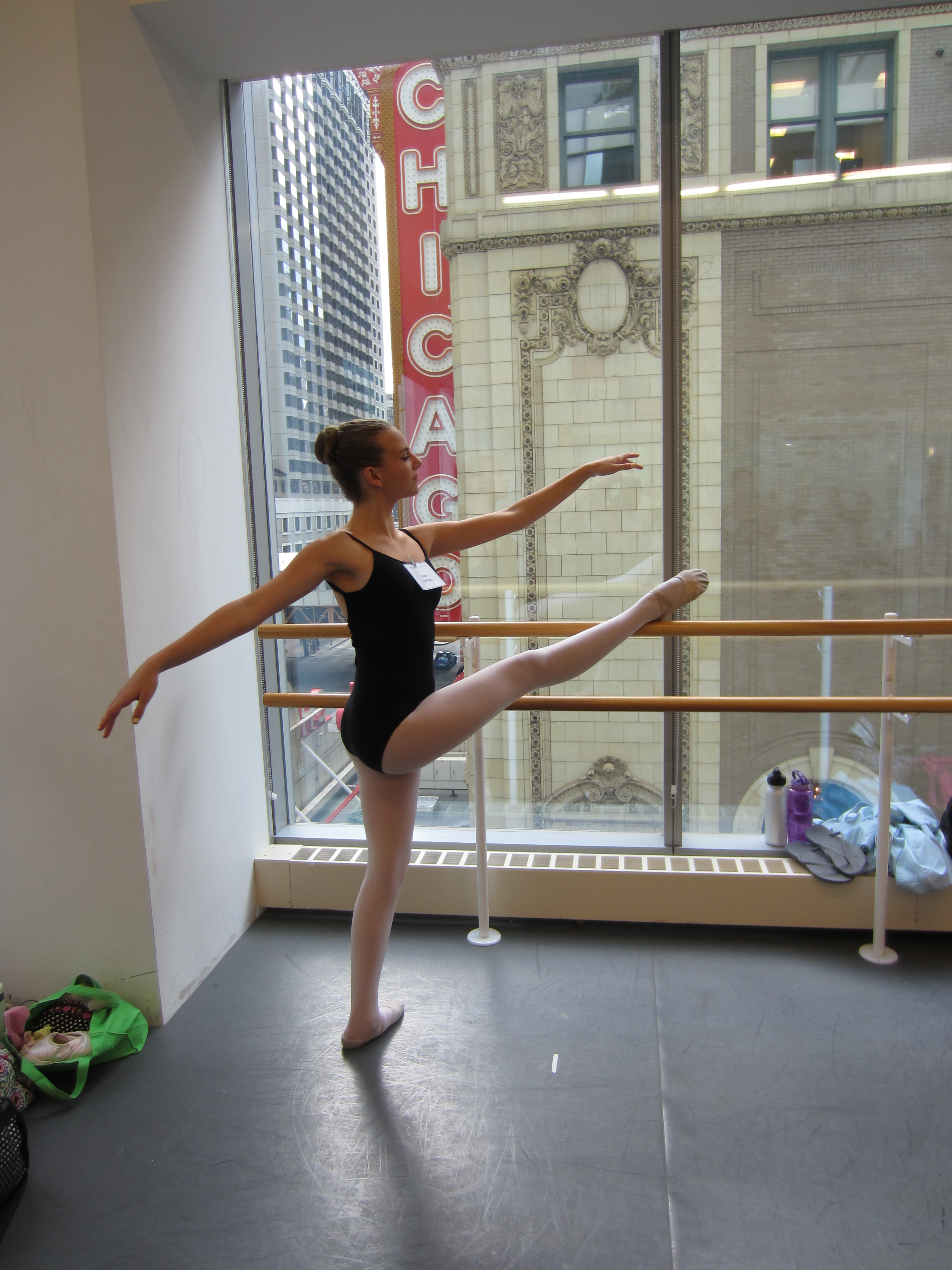 Kate has her front leg on the ballet bar in front of a window looking out on the iconic Chicago Marque sign.