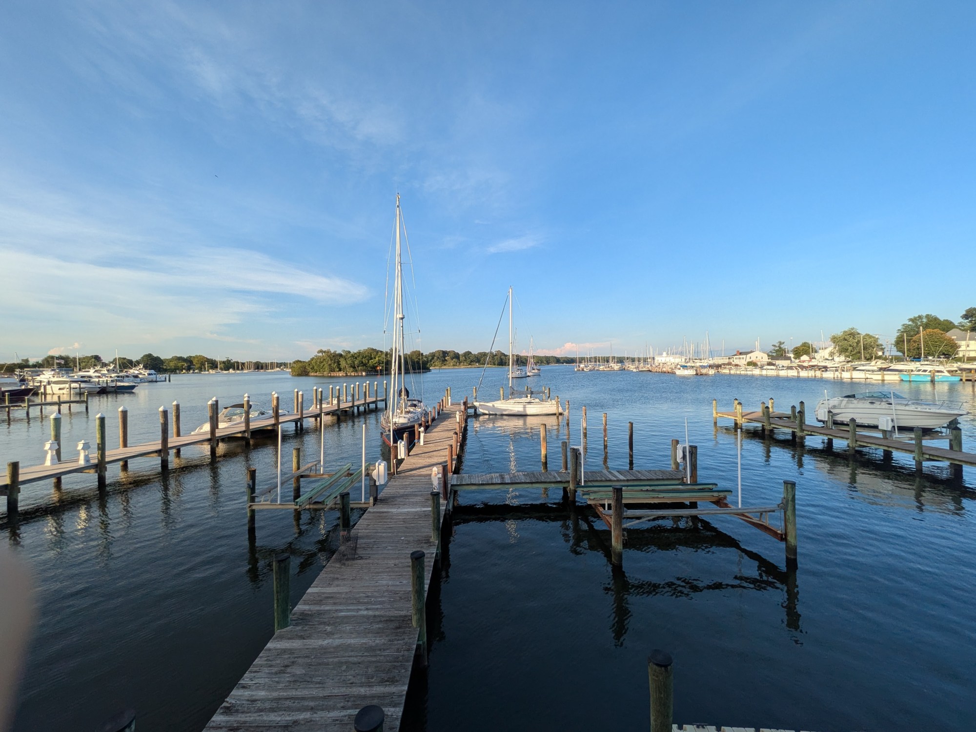 A wooden dock with two sailboats on a calm bay from the ocean.